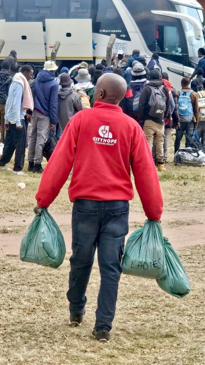 A CityHope Disaster Relief volunteer carries bags of care supplies toward buses transporting foreign nationals.