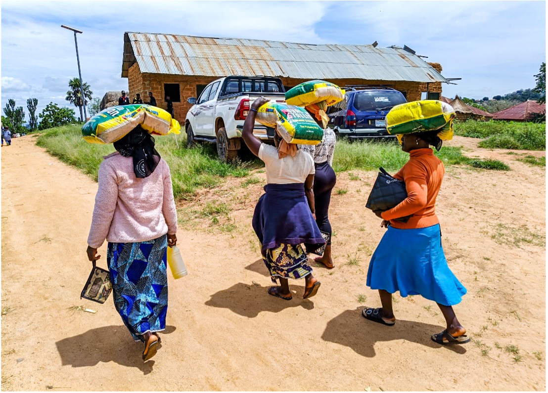 Women walk along a dirt road carrying food parcels on their heads after a CityHope distribution in Plateau State.