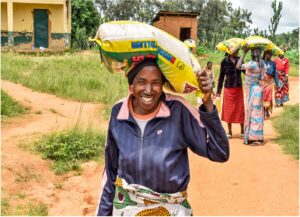 A woman smiles as she carries a 25kg bag of rice on her head, walking home from a CityHope food distribution in Nigeria.