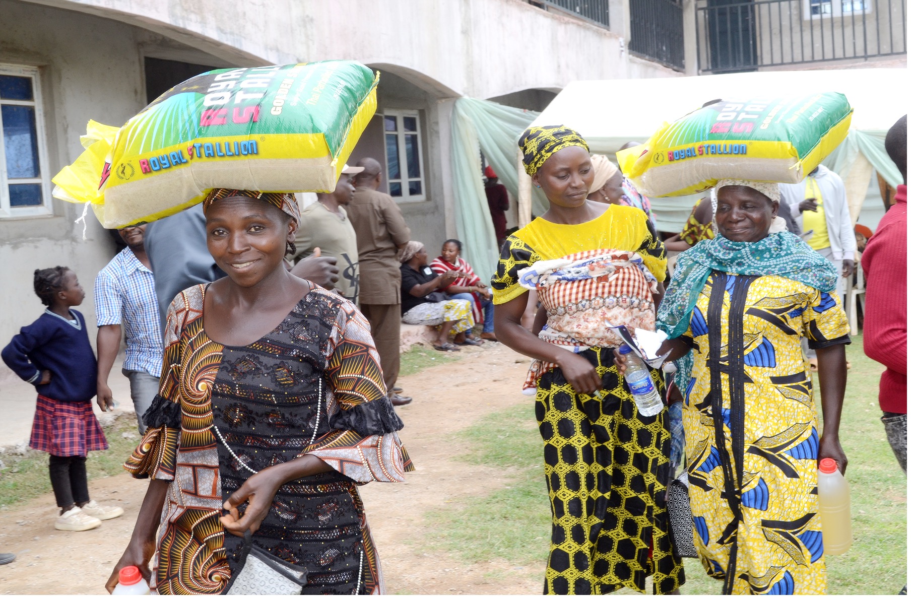 Three women carry rice and vegetable oil home after receiving food parcels in Kaduna State, Nigeria.